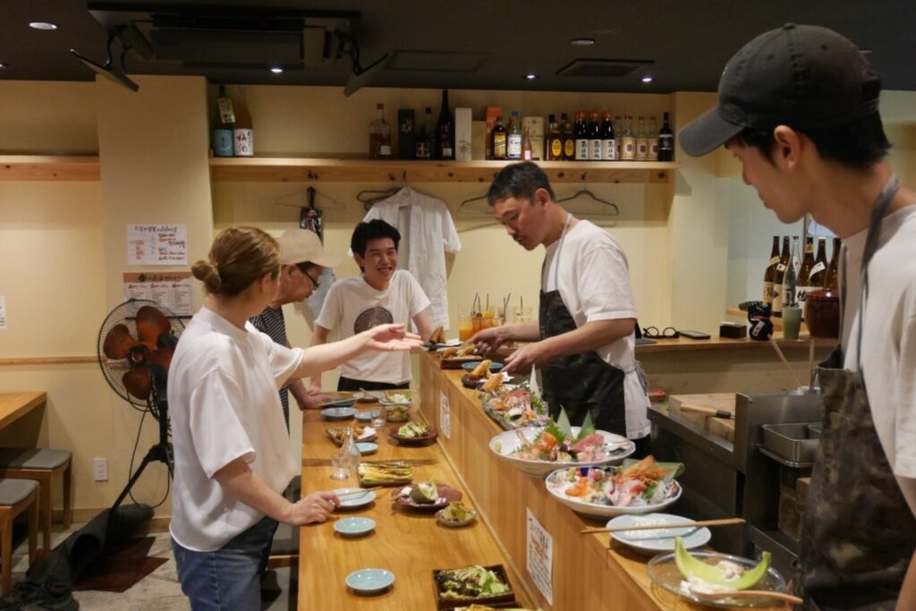 飲食店「吉」のカウンターで、お客様に料理を提供する小峰丈晴さん
