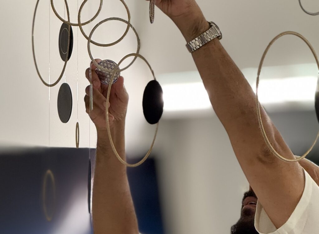 Simon Alcantara adjusting a suspended installation composed of circular forms and hanging elements.
