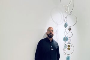 Simon Alcantara standing beside a suspended installation of circular forms and translucent elements.