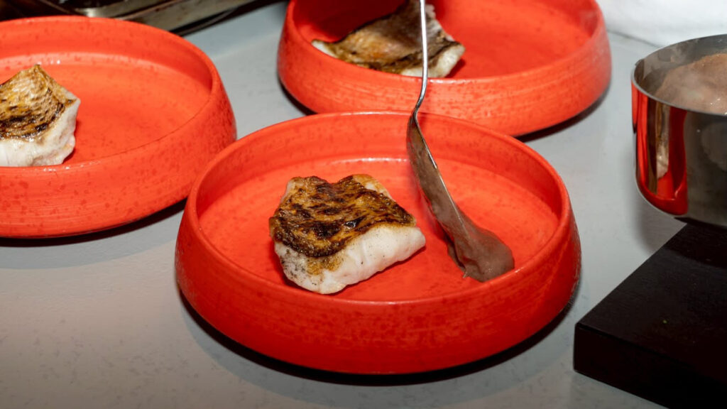 RÉJOUISSANCEの厨房で赤い器に盛り付けられた魚料理を仕上げる様子