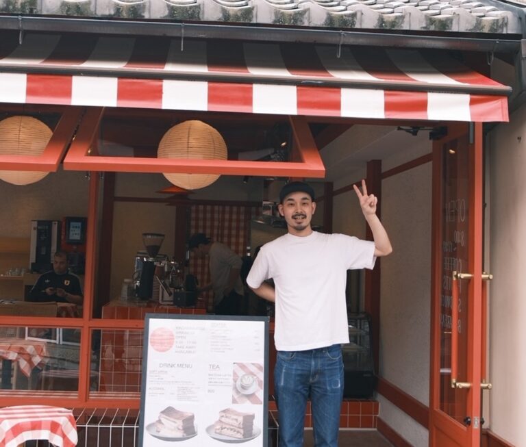 赤と白のストライプの日よけがある禁断果実・銀閣寺店の入口で、笑顔でピースサインをするオーナーの篠崎光希さん。