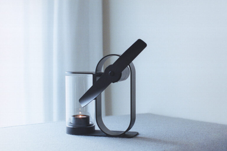 Lei non electric aroma diffuser with a lit candle beside a sheer curtain.