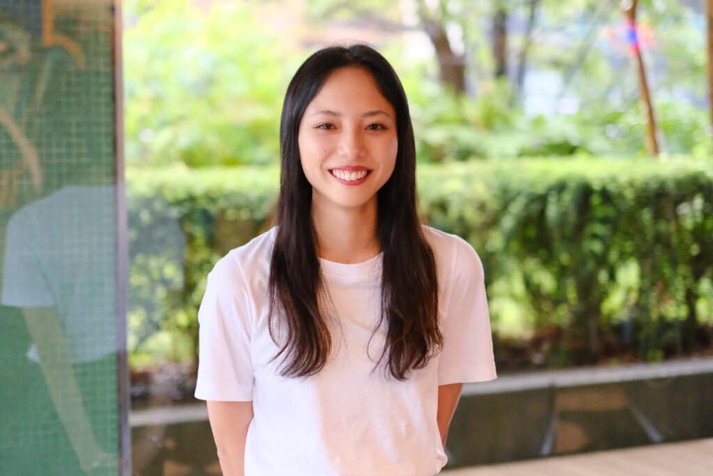 Palm Springs Day Camp Resort責任者の山口彩奈さん。白いTシャツ姿で、緑を背に微笑んでいる