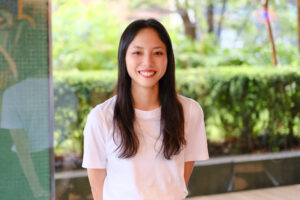 Palm Springs Day Camp Resort責任者の山口彩奈さん。白いTシャツ姿で、緑を背に微笑んでいる