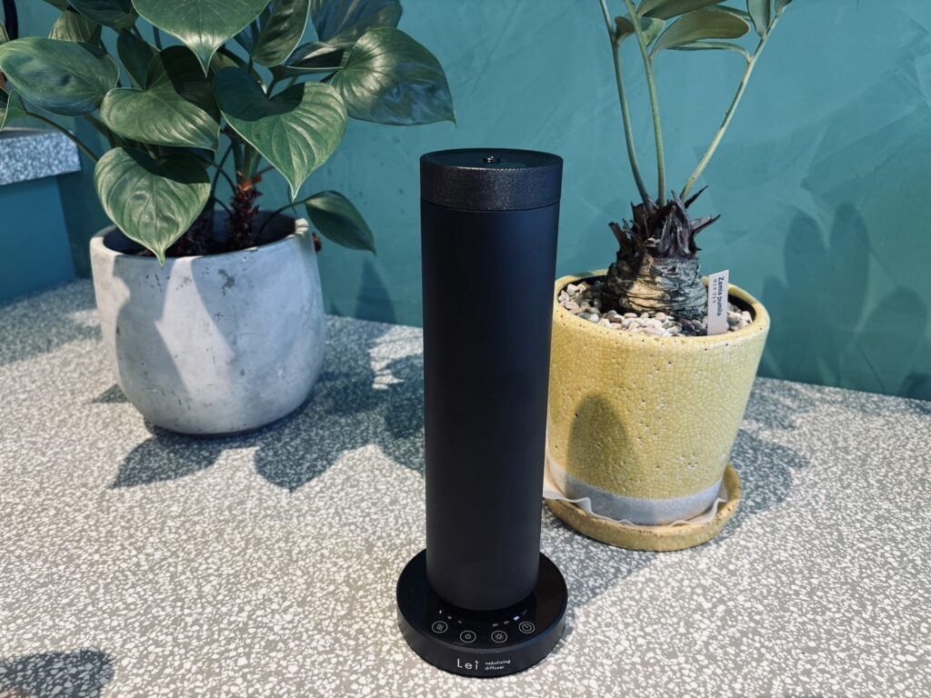 Palm Springsの入口カウンターに置かれた、黒い円筒形のLei業務用ディフューザー。両脇に観葉植物の鉢がある