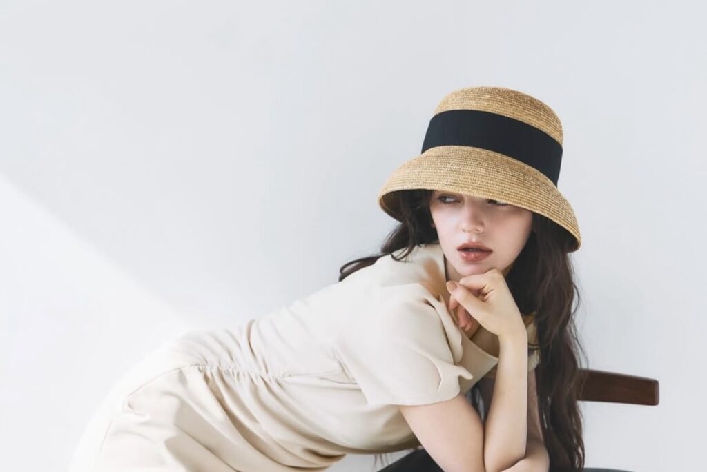 Adelaide Mati con cappello di paglia e abito bianco, seduta su una sedia